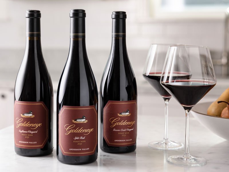 Three bottles of Goldeneye Pinot Noir with two glasses of wine