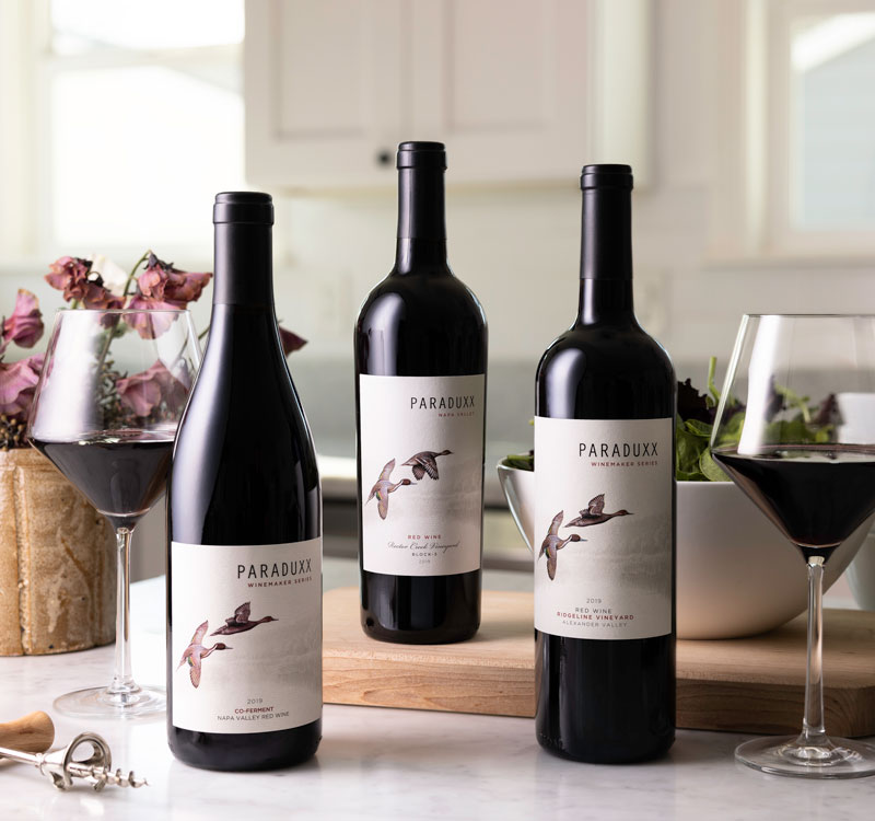 Three Paraduxx wines on a kitchen counter with two glasses of wine