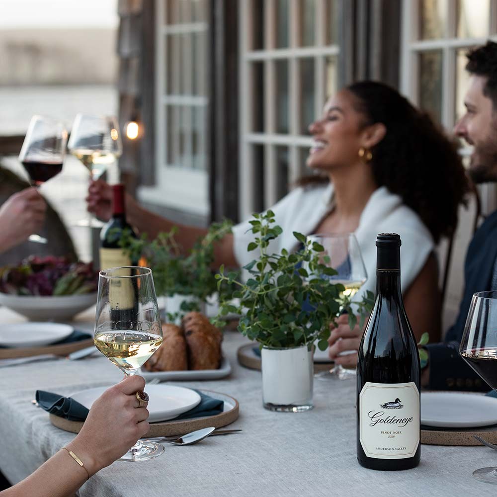 Two Duckhorn Portfolio wines on a table with people enjoying wine and food
