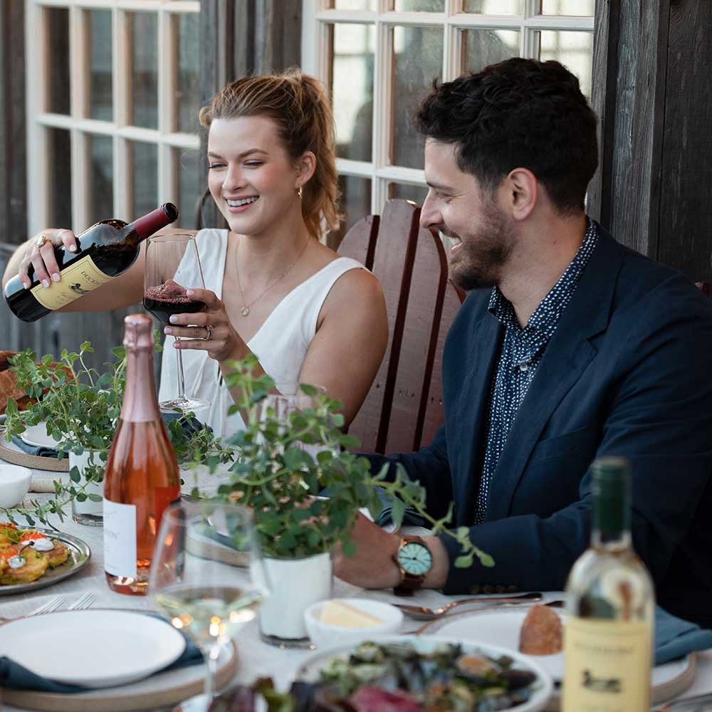 Three Duckhorn Portfolio wines on a table with people enjoying wine and food